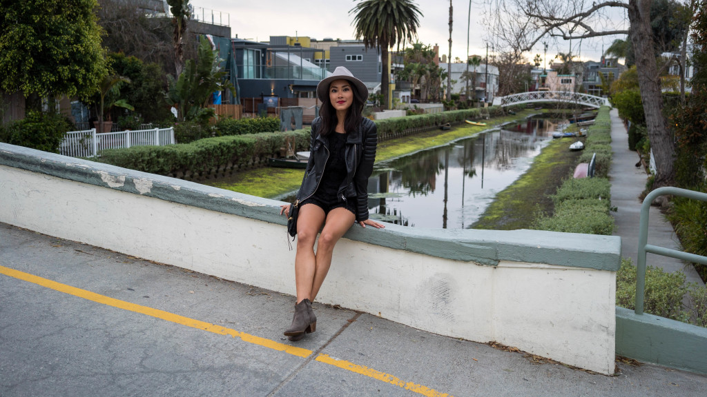 Woman wearing black romper and leather jacket sitting near the river