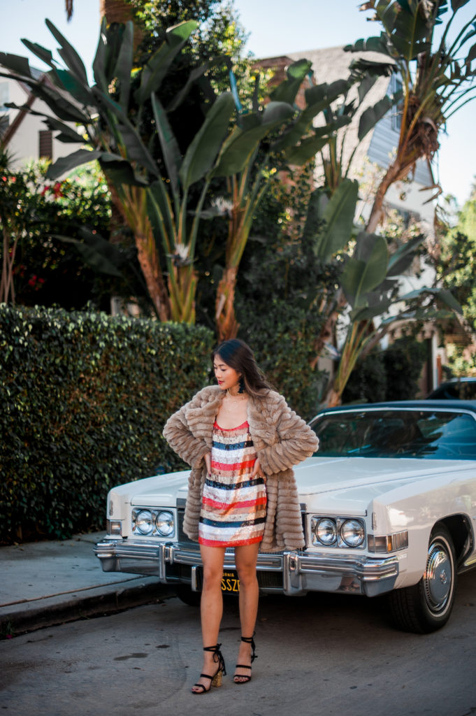 woman standing near a car and wearing sequence dress and coat 